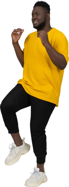 Vista de três quartos de um jovem de pele escura em uma camiseta amarela levantando a perna