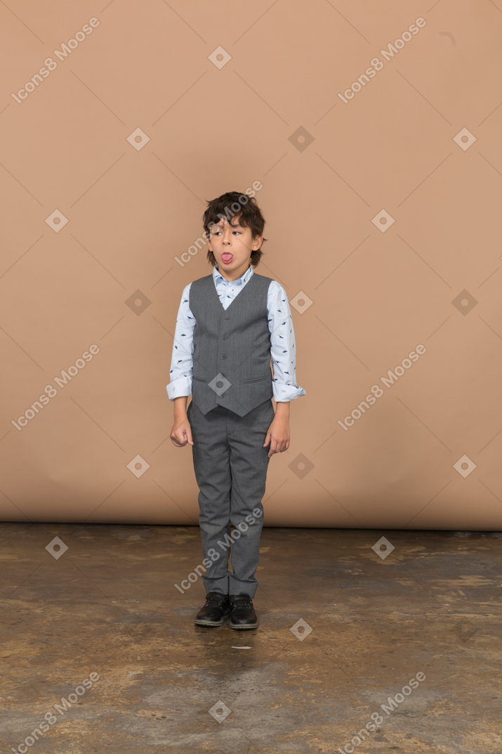 Frente a un niño en traje gris mostrando la lengua