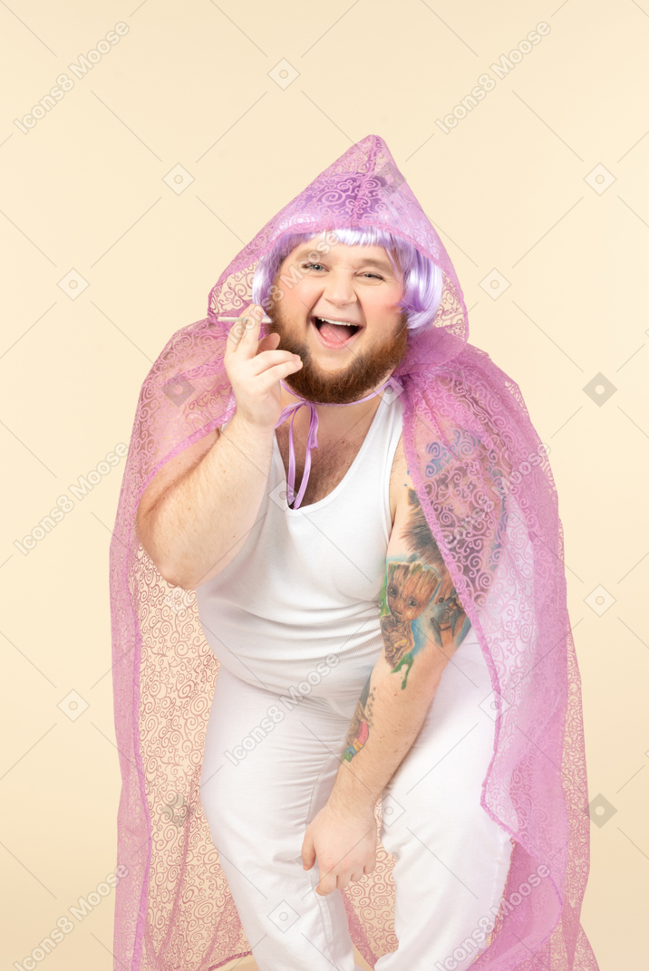 Laughing young overweight man in fairy cape holding a cigarette