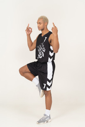 Dreiviertelansicht eines meditierenden jungen männlichen basketballspielers mit mittelfinger
