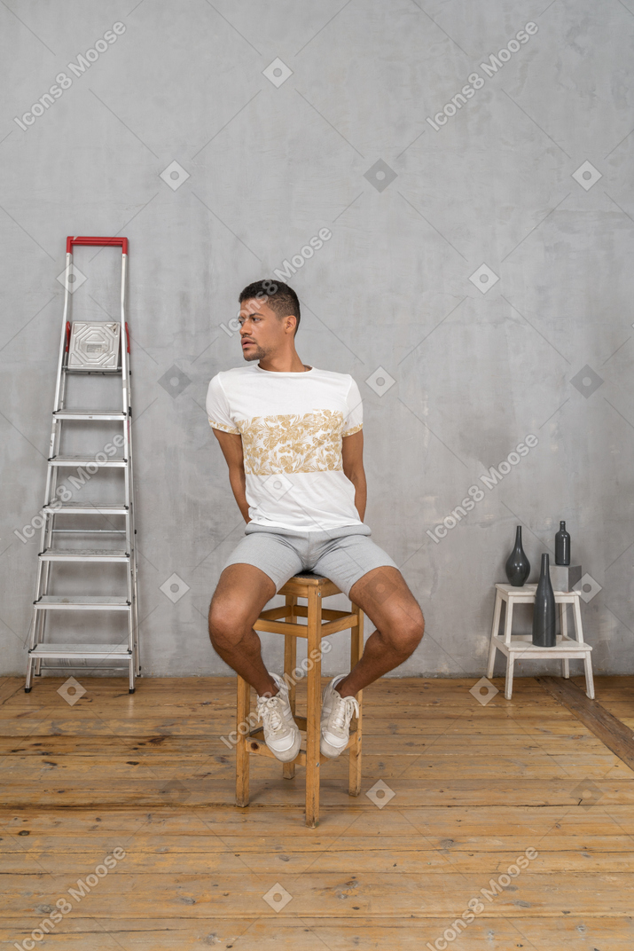 Young man sitting on stool and looking to the left