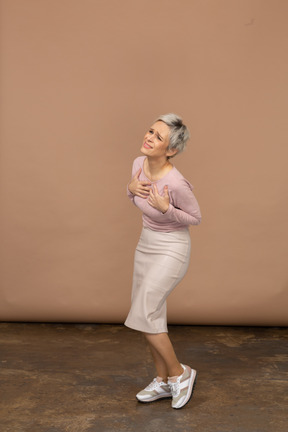 Vista lateral de una mujer emocional en ropa casual de pie con las manos en el pecho