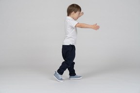 Vista lateral de um menino andando com as mãos estendidas
