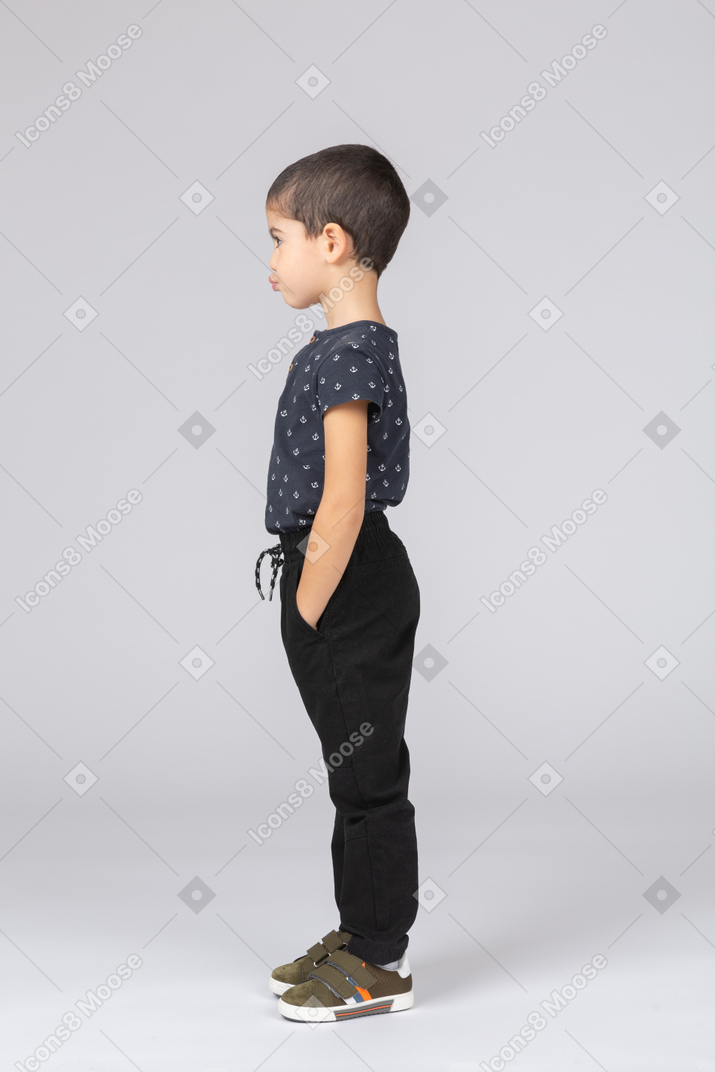 Side view of a cute boy posing with hands in pockets and making faces