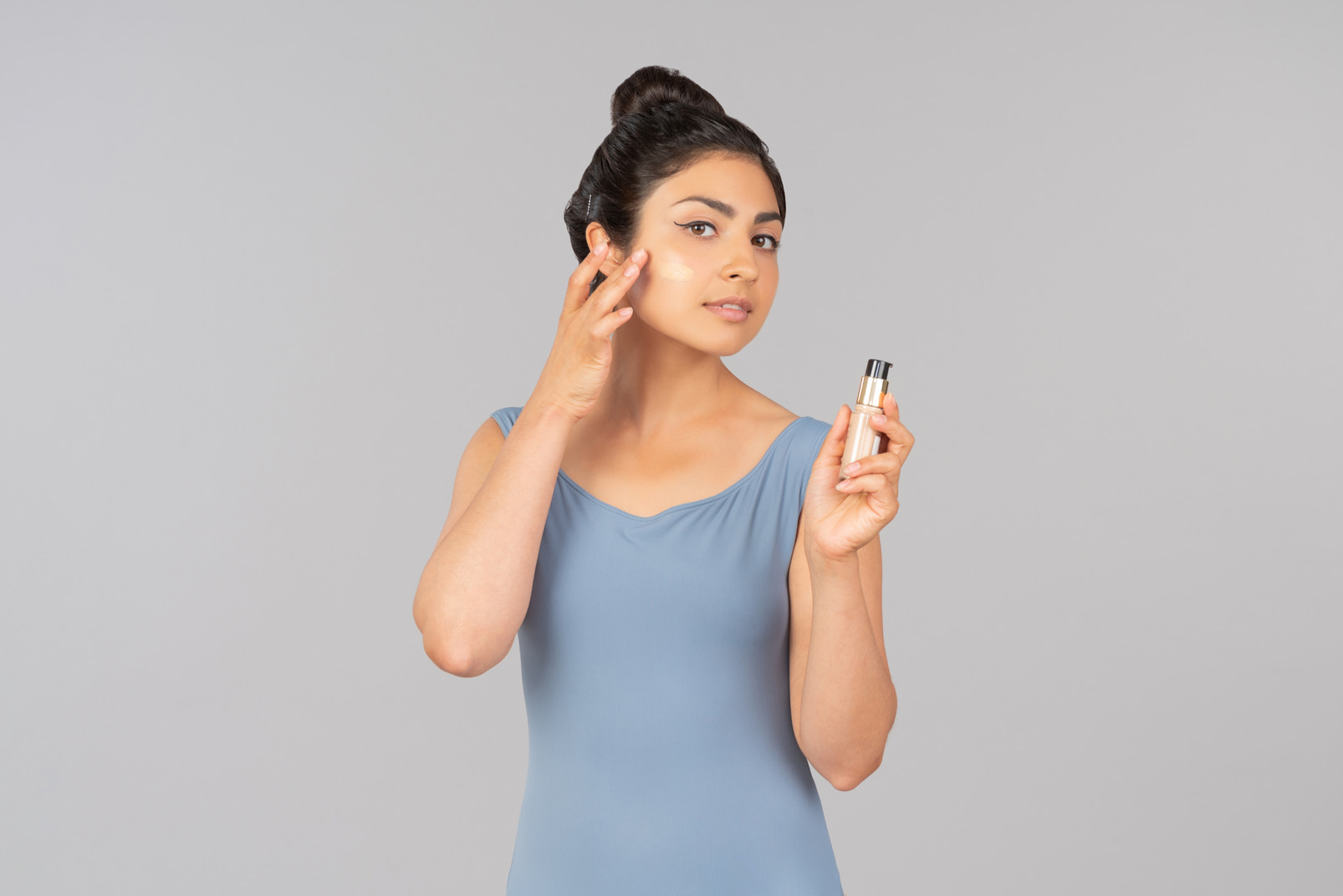Young indian woman with tonal foundation on her face holding tonal foundation bottle
