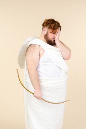 Ashamed big guy dressed as a cupid closing face with a hand