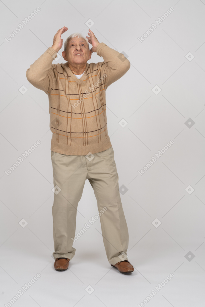 Front view of an impressed old man standing with raised hands and looking up