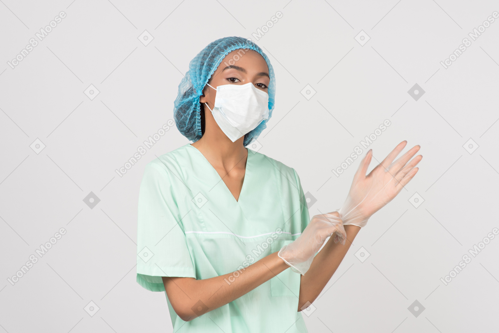 A young woman in a surgical hat and a face mask putting on gloves