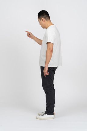 Side view of a man in casual clothes pointing at something and looking down