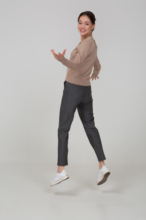 Three-quarter back view of a smiling jumping lady in beige pullover turning away