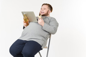 Offre homme barbu tenant un ordinateur portable sur le ventre, regarder un film et avoir des frites et de la bière