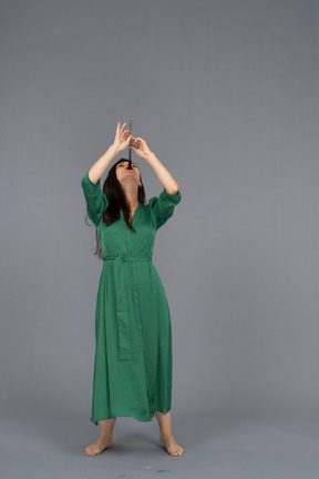 Vista frontal de una joven en vestido verde tocando la flauta mientras se inclina hacia atrás