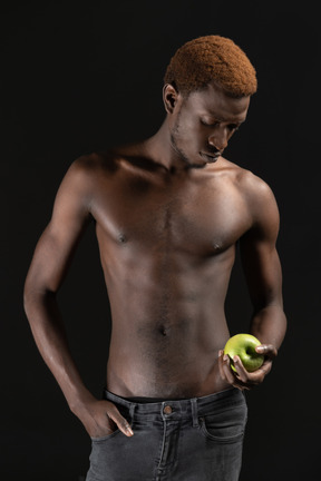 Muscular thoughtful man holding an apple in the dark