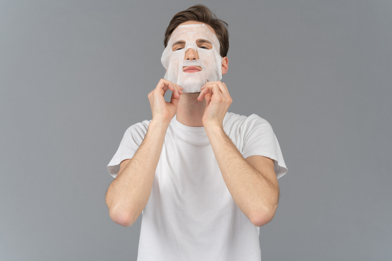 Front view of a young man putting on facial mask