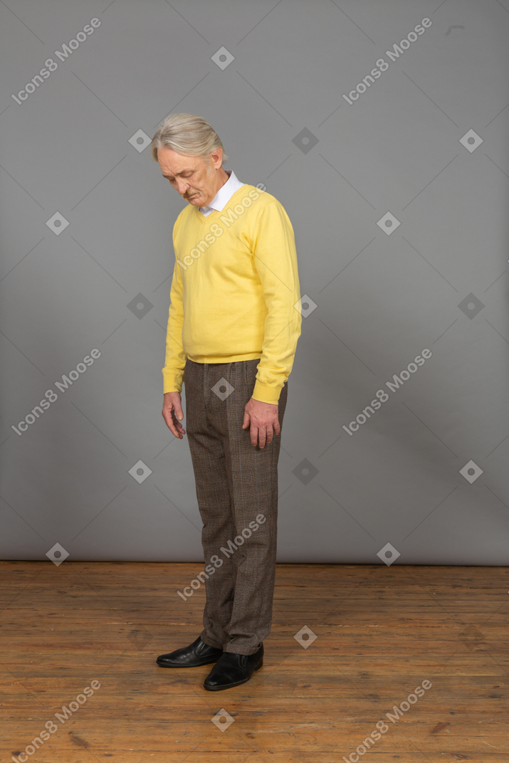 Three-quarter view of an old sad man in yellow pullover bending down with his eyes closed