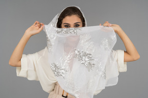 Cheerful young arab woman covering face with white shawl with silver embroidery