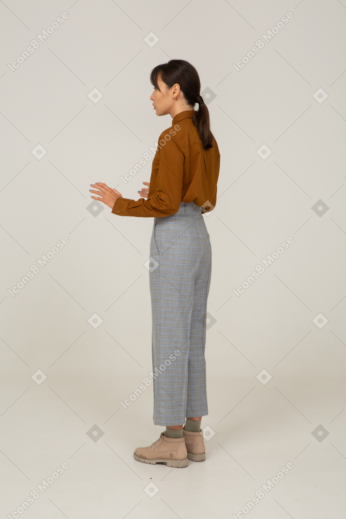 Three-quarter back view of a young asian female in breeches and blouse raising her hands