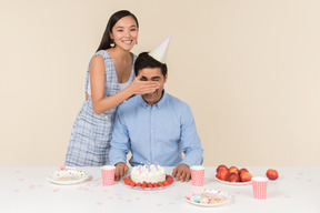 Young asian woman closing eyes to a caucasian guy sitting in front of cake