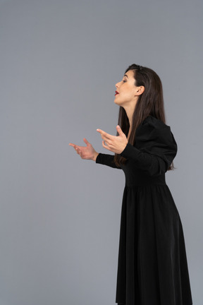 Vista laterale di una giovane donna gesticolante in un abito nero