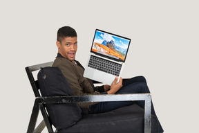 坐在沙发上拿着笔记本电脑的年轻人的侧视图