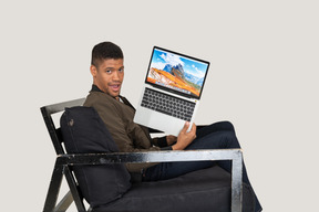 Side view of young man sitting on a sofa and holding a laptop