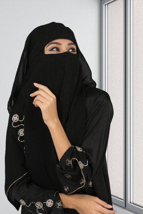 A woman in a black hijab is looking out a window