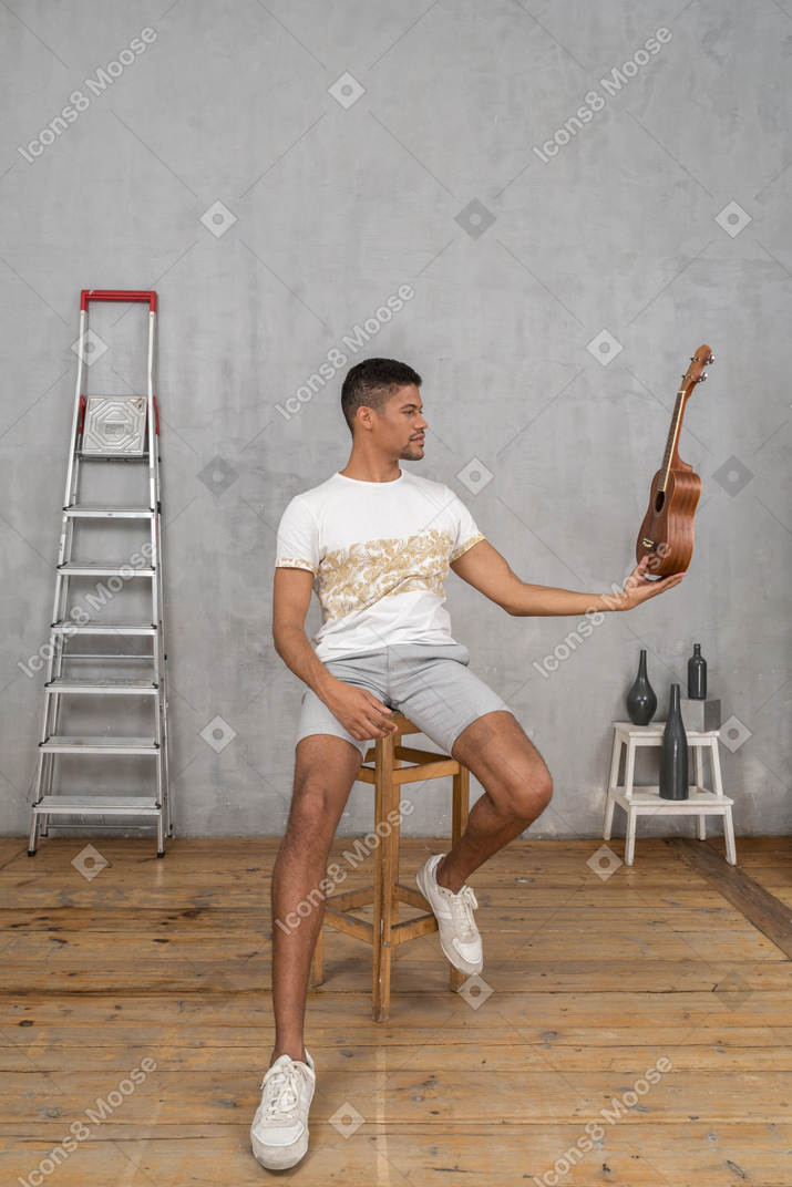 Vista frontale di un uomo su uno sgabello che tiene un ukulele come il teschio del villaggio