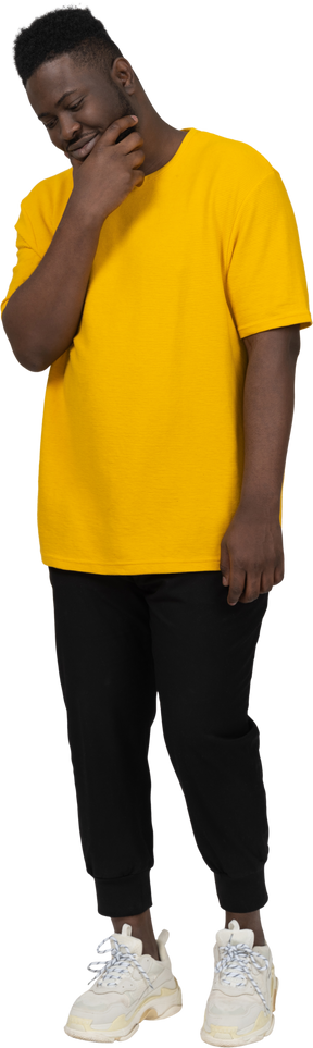 Vista de três quartos de um jovem adivinhando homem de pele escura em uma camiseta amarela tocando o queixo