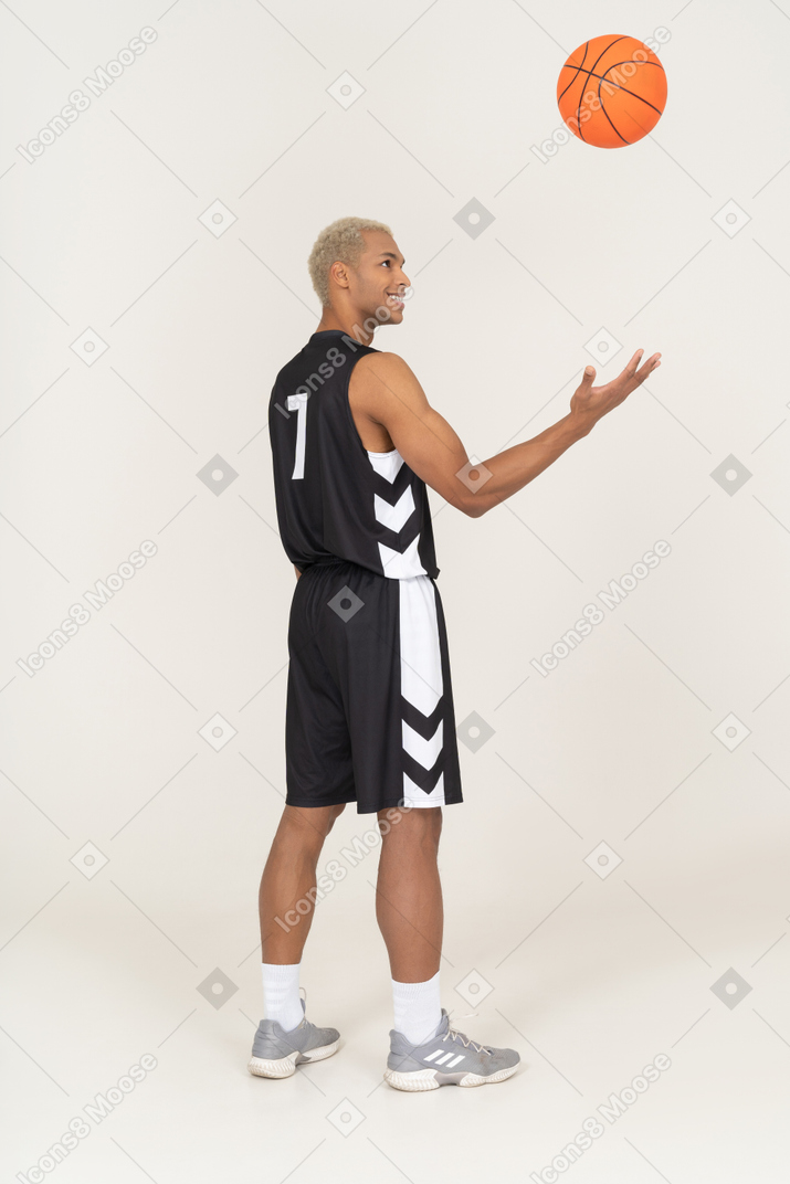 Vista posterior de tres cuartos de un sonriente joven jugador de baloncesto lanzando una pelota