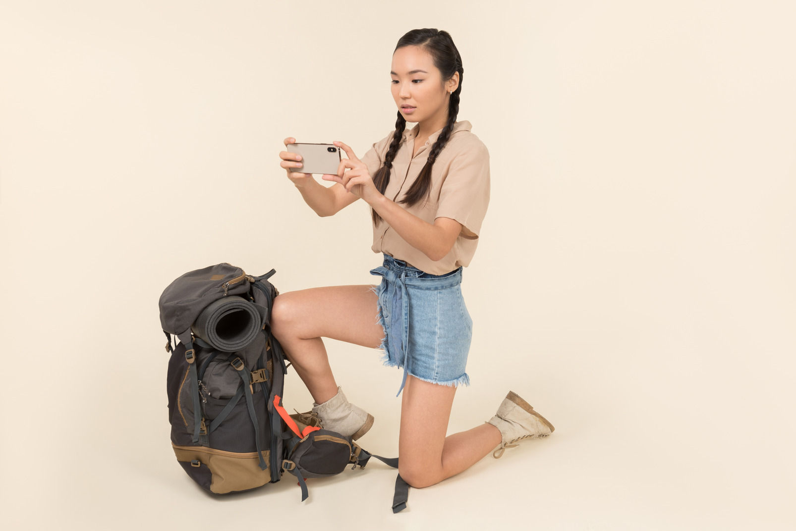 Outraged young asian woman standing near backpack and taking picture with smartphone