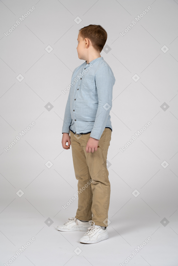 Side view of a boy in casual clothes standing still and looking aside