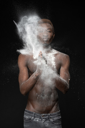 A muscular man making a clap with a bursting flour in the dark