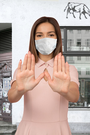 Mujer joven con mascarilla que muestra el signo de la mano de parada