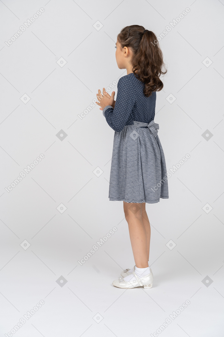 Vista traseira de três quartos de uma garota juntando as palmas das mãos