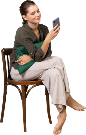 Front view of a smiling young woman sitting on a chair while checking her phone