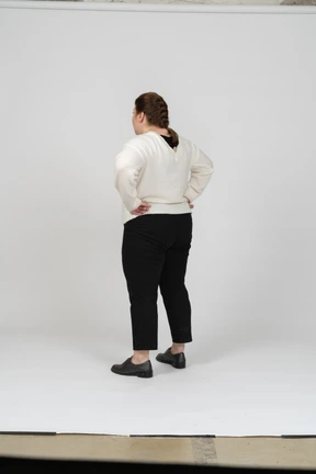 Rear view of a plump woman in casual clothes standing with hands on hips
