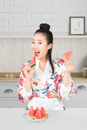 Asian woman eating watermelon in the kitchen