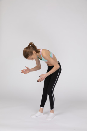 Three-quarter view of a teen girl in sportswear bending over and raising her hands