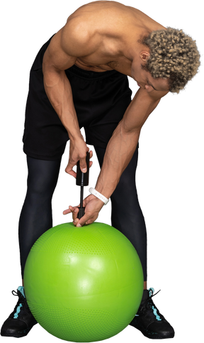 Front view of a shirtless afro man inflating a gym ball