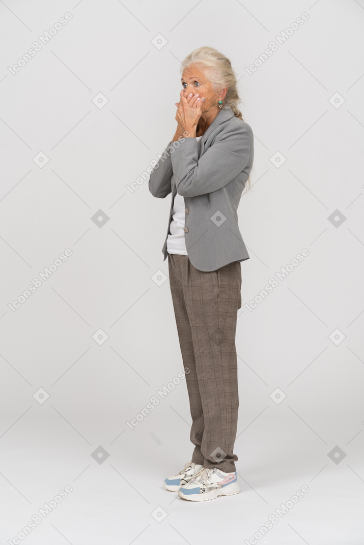 Side view of a scared old lady in suit covering mouth with hands