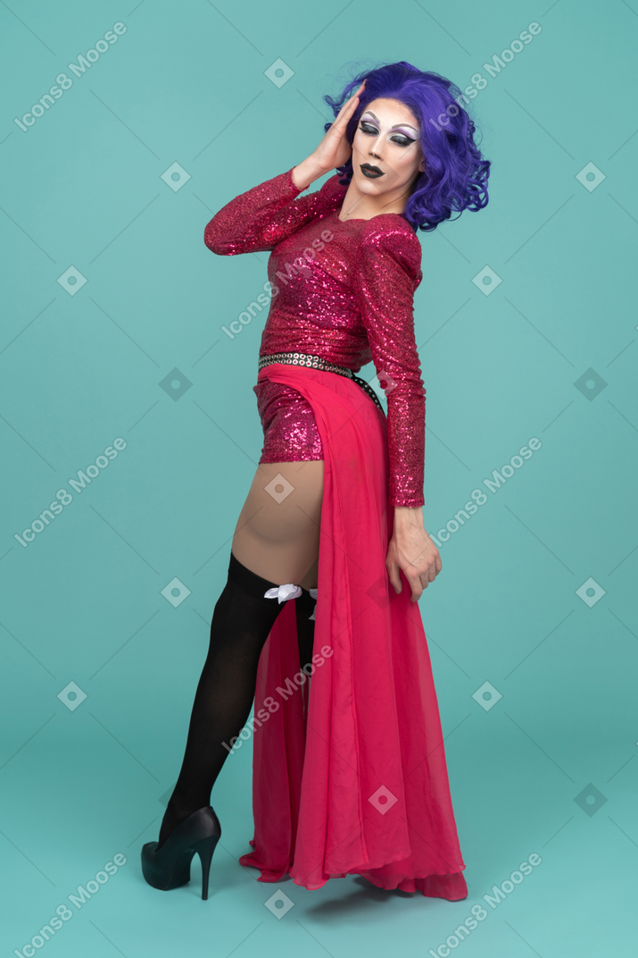 Drag queen in pink dress turning around with hand next to face & closed eyes