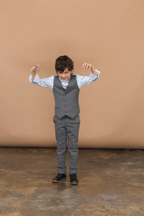 Vista frontal de un chico lindo con traje gris asustando a alguien