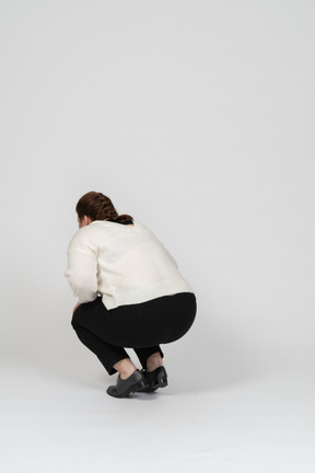 Rear view of a plump woman in casual clothes squatting
