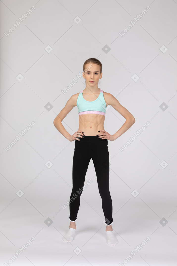 Vista frontal de una jovencita en ropa deportiva poniendo las manos en las caderas