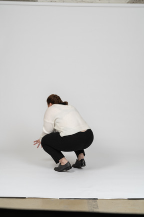 Rear view of a plump woman in casual clothes squatting