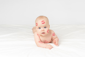 Baby mit roten lippenstiftküssen, die auf magen liegen