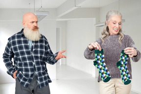 A bald old man with a gray beard looking to an old lady amazedly while she is holding a couple of green socks in her hands