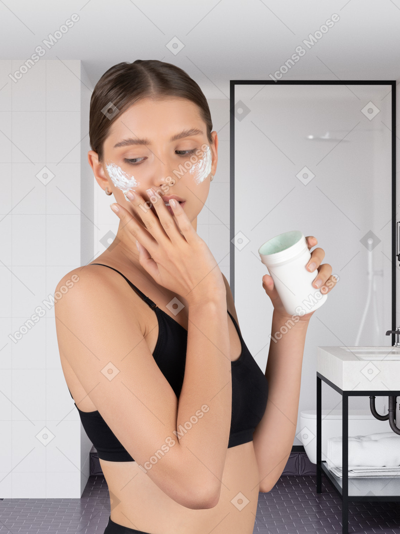 A woman with moisturizer on her face holding a jar