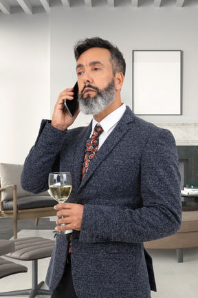 A man holding a glass of wine while talking on a cell phone