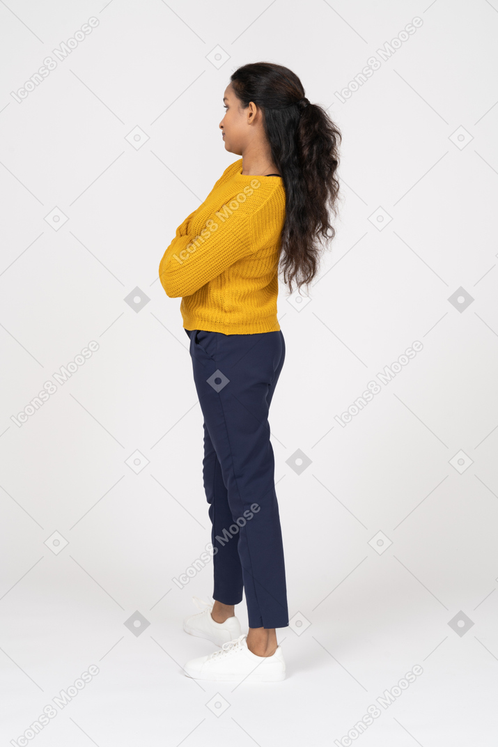 Vista lateral de uma garota com roupas casuais posando com os braços cruzados